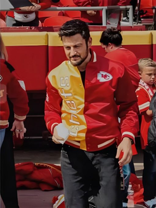 Man wearing a red and yellow sports jacket with a logo, standing in a crowd.