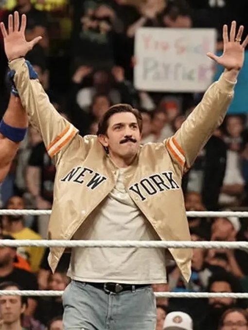 Man in a beige jacket with 'New York' text, standing in a wrestling ring with arms raised.