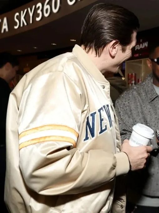 Person wearing a beige jacket with 'New' branding, holding a white cup in an indoor setting.
