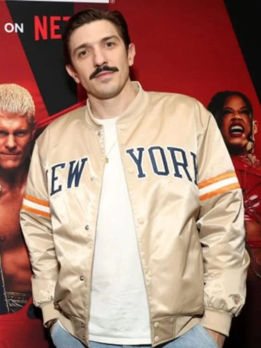 Man wearing a 'New York' jacket in front of a promotional backdrop with characters from a show or movie.