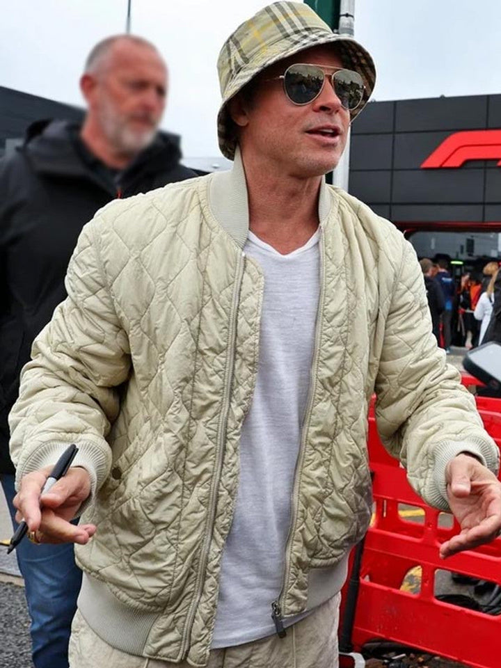 Man wearing a beige quilted jacket and hat with sunglasses, standing outdoors.