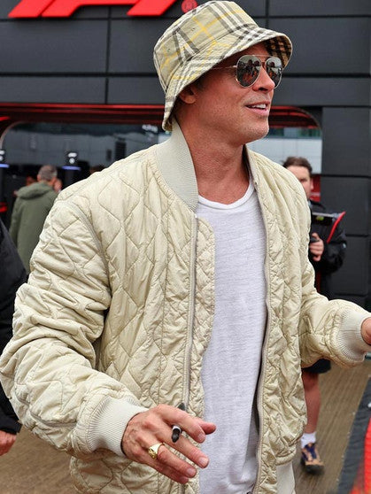 Man wearing a beige quilted jacket, plaid bucket hat, and sunglasses outdoors.
