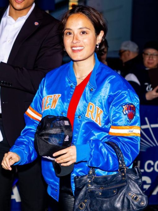 Person wearing a blue jacket with 'New York' text, holding a cap and handbag, with a blurred background.