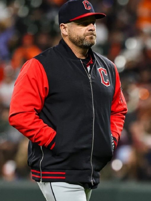 Person wearing a black and red sports jacket with a logo, standing on a field.
