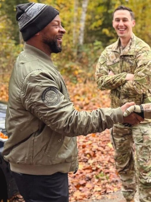 Two men shaking hands outdoors with autumn foliage in the background