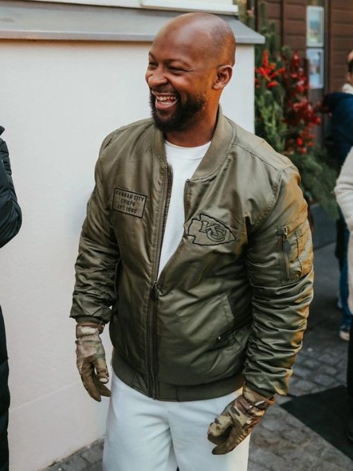 Man wearing a green bomber jacket with patches, standing outdoors.
