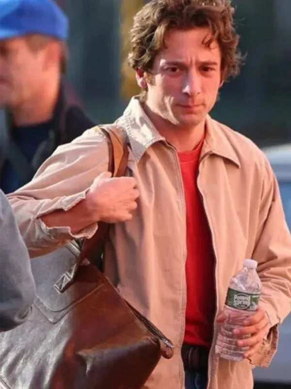 Man holding a water bottle and a bag, with another person partially visible in the background.