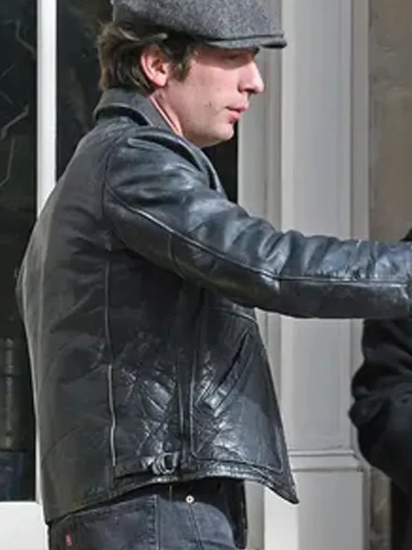 Person wearing a black leather jacket and cap outdoors