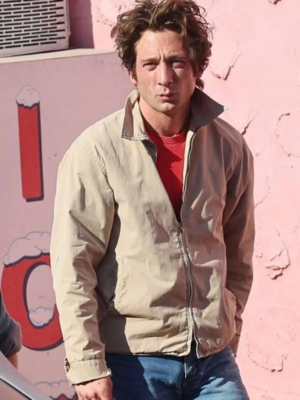 Man wearing a beige jacket over a red shirt against a pink wall with ice cream graphics.