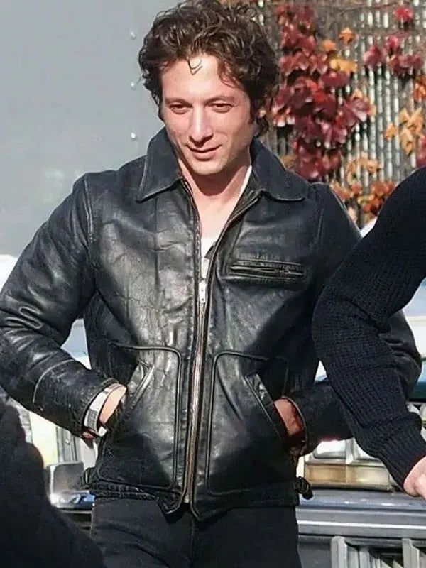 Man wearing a black leather jacket outdoors with autumn leaves in the background