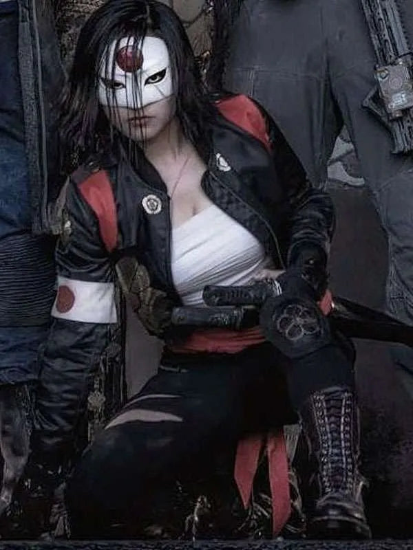 Person in a detailed costume with black and red accents, sitting on a dark surface.