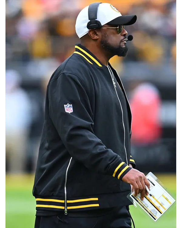 Person wearing a black jacket with yellow accents and an NFL logo on a sports field.