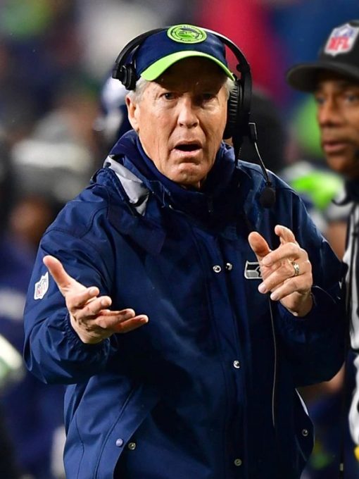 Person in a blue jacket and cap with a headset, likely a coach, in a sports setting.