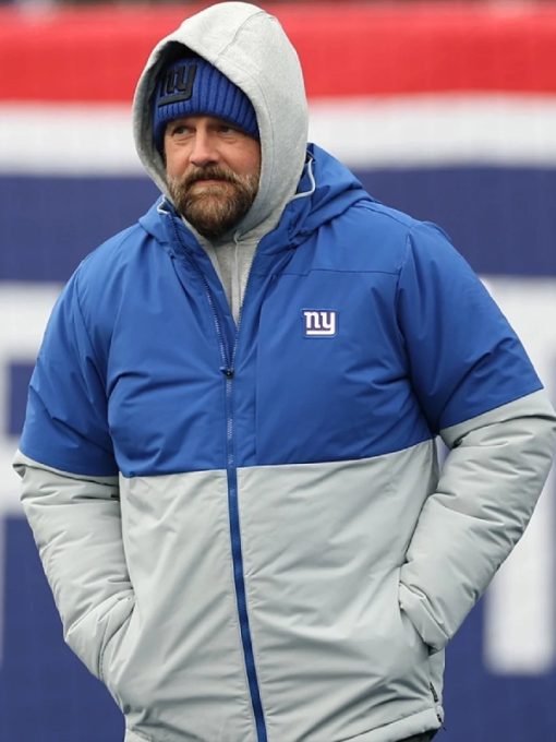 Person wearing a blue and gray jacket with a logo, standing against a red and white background.