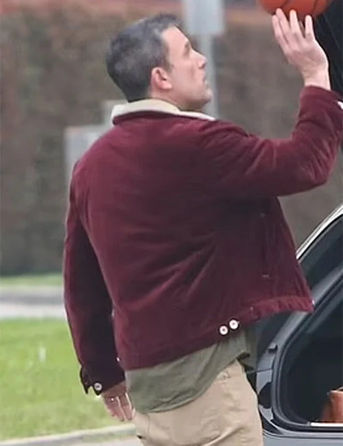 Man in a maroon jacket reaching into a car trunk outdoors