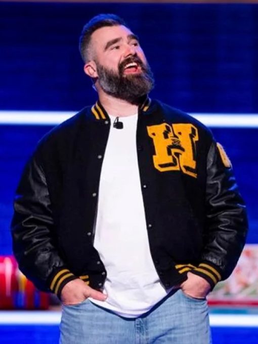 Man wearing a black varsity jacket with yellow lettering on a stage with blue background