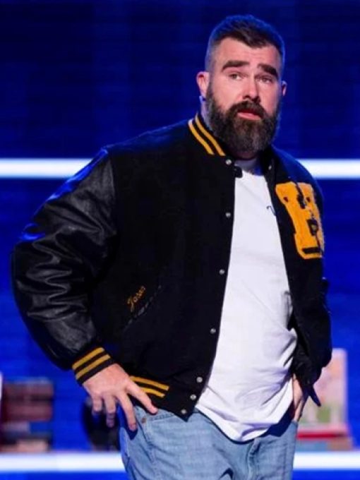 Man wearing a black varsity jacket with yellow accents on a blue background